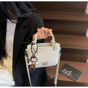 Detail of white mini bucket bag with gold lettering, pearl chain, and cute doll charm