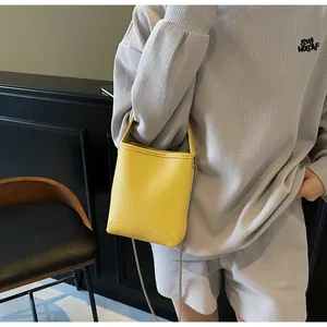 Detail van de felgele bucket bag van leer met litchi-textuur en metalen ketting