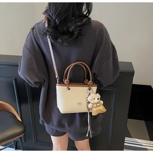 Detail of beige woven bucket bag with brown leather trim and a cute teddy bear charm
