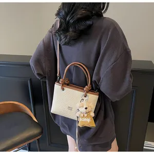 Detail shot of the beige woven bucket bag with leather trim and bear charm on a model