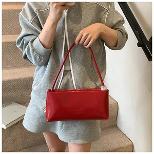 Detail of red glossy leather handbag with subtle logo engraving shown in street style shot