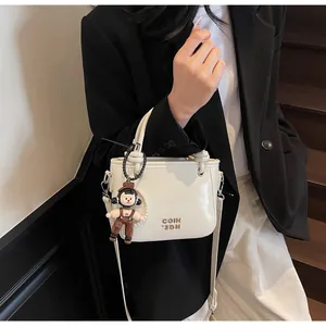 Close-up of white glossy bucket bag with metal handle and cute cartoon charm