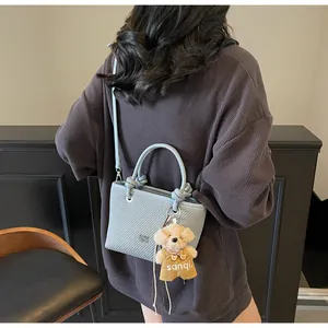 Detail of light blue woven crossbody bag with knot handles and cute bear charm