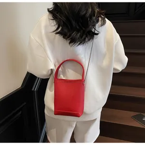 Detail van rode bucket bag met litchi-textuur en zilveren ketting op model