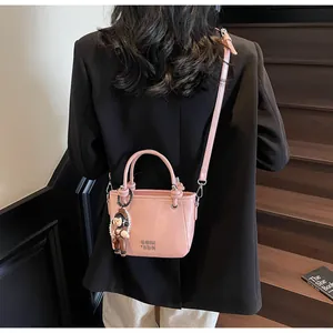 Detail of pink leather bucket bag with metallic logo, doll charm and pearl chain strap