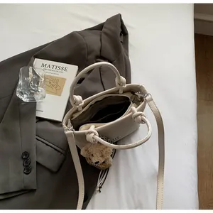 Close-up of cream woven bucket bag with dual handles and cute brown bear pendant detail