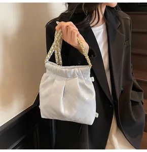 Detailed view of white quilted bucket bag with woven metal chain strap held by model
