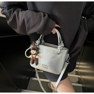 Detail of silver metallic bucket bag with cute doll charm and knotted handle design