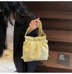 Close-up of a cream quilted bucket bag with chain strap held by a model on stairs