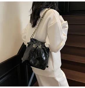 Detailed view of black quilted bucket bag with gold chain strap and glossy leather finish