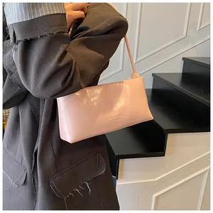 Close-up of pink glossy baguette bag with branded logo worn by a model in a suit