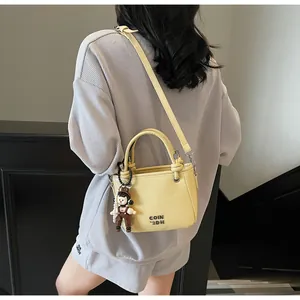 Detail of light yellow leather bucket bag with cute doll charm and branded engraving