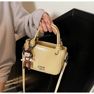 Detail of cream mini bucket bag featuring metal logo and pearl cartoon charm