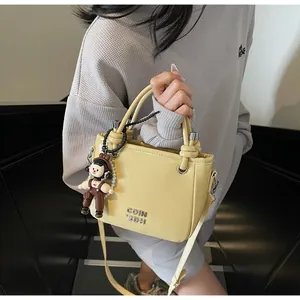 Detail of pale yellow bucket bag featuring COIN 2DH metal logo and cute doll charm