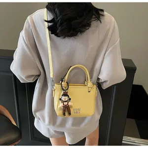 Detailed close-up of yellow bucket bag with metal letters and cute doll charm accessory