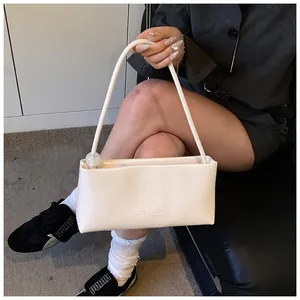 Close-up of cream faux leather baguette bag with cylindrical strap and clear bead detail