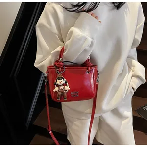 Detail of red leather bucket bag with metal logo and cute cartoon doll pendant
