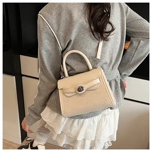 Detail view of cream crossbody bag with embossed bear patterns and metal twist lock