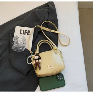 Detail of light yellow leather bucket bag with 3D logo, pearl strap and cute doll charm