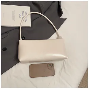 Close-up of cream faux leather baguette bag with minimalist brand logo and orb detail