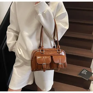 Brown glossy tote bag with dual front buckle pockets on a rustic wooden staircase