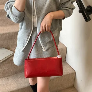 Red rectangular patent leather shoulder bag with transparent sphere charm on gray outfit