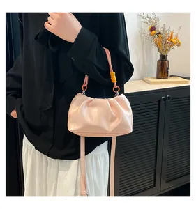Detail of light pink ruched cloud handbag with orange decorative ring and crossbody strap