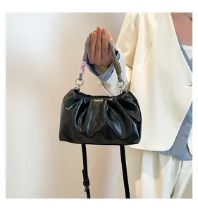 Close-up of black pleated cloud bag with unique floral knot handle and glossy finish
