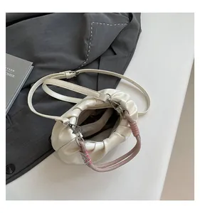 Detail view of cream pleated dumpling bag featuring colorful woven knot handle and shoulder strap
