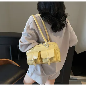 Detail of a glossy pale yellow bowling bag with dual front pockets on a model shoulder