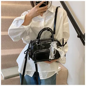 Detalle del bolso de charol negro brillante con lazo de encaje blanco y perlas