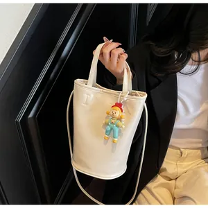 Detail van crème bucket bag met modieuze reliëf en schattige cartoon bedeltje