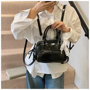 Detalle de una mini mochila negra brillante con colgante de encaje y doble asa