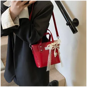 Dettaglio mini borsa tote in vernice rossa con fiocco in pizzo e ciondolo a cuore