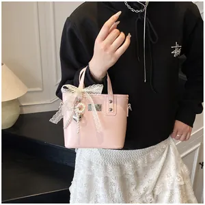 Dettaglio borsa in pelle verniciata rosa con fiocco in pizzo e ciondolo a cuore