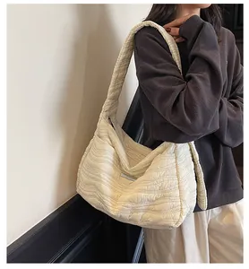 Detail of a large cream pleated shoulder bag with wavy quilted texture on a model