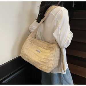 Détail du sac bandoulière matelassé beige avec coutures ondulées et plaque métallique