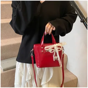 Dettaglio mini borsa rossa in vernice con fiocco in pizzo bianco e ciondolo di perle