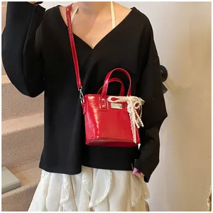 Dettaglio borsa a secchiello in pelle verniciata rossa con fiocco in pizzo e perle su modella
