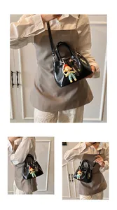 Detail of black patent leather mini bucket bag with glossy finish and cute doll pendant