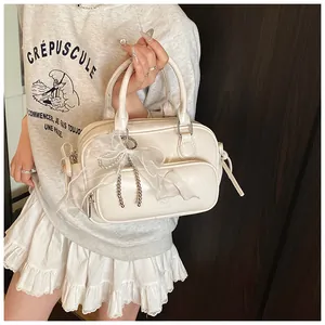 Detalle de un bolso Boston crema con lazo de encaje y cadena de perlas en una modelo real