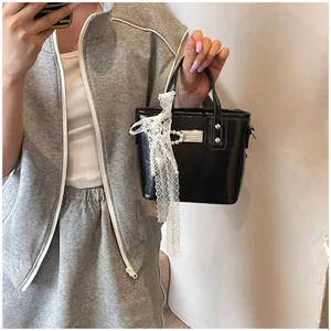 Dettaglio mini borsa nera lucida con nastro in pizzo e ciondolo di perle