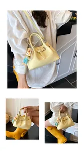 Pale yellow bucket bag shown in cross-body and hand-held style with pearl charm details