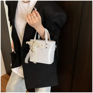 Dettaglio borsa a secchiello bianca con elegante fiocco in pizzo perlato e finitura lucida