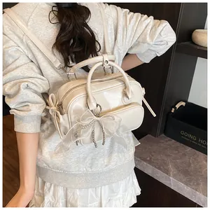 Detalle de una mochila de cuero sintético blanco crema con lazo y cadena de perlas