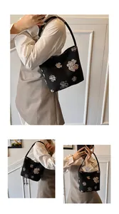 Detail of minimalist black hobo bucket bag with elegant beige floral embroidery patterns