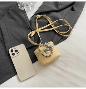 Detail view of mini yellow leather bag with silver beaded handle next to a smartphone