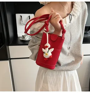 Detail of red lychee textured phone bag with cute duck charm and slim shoulder strap