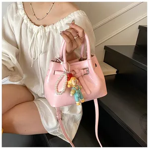 Pink glossy pleated bucket bag with pearl chain and doll pendant detail shown on a model
