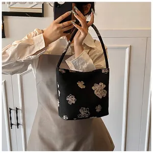 Detail of black canvas bucket bag with beige floral embroidery held by a model